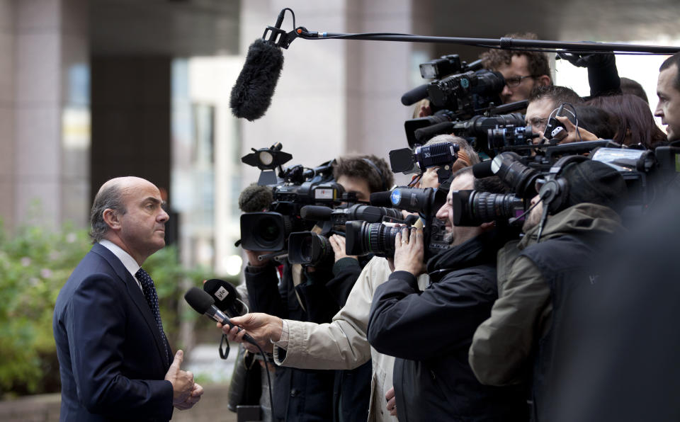 Spain's Economy Minister Luis de Guindos, left, speaks with the media as he arrives for a meeting of eurogroup finance ministers at the EU Council building in Brussels on Monday, Nov. 26, 2012. Eurozone finance ministers are set to meet in Brussels on Monday to discuss the next installment of bailout money for debt-laden Greece. (AP Photo/Virginia Mayo