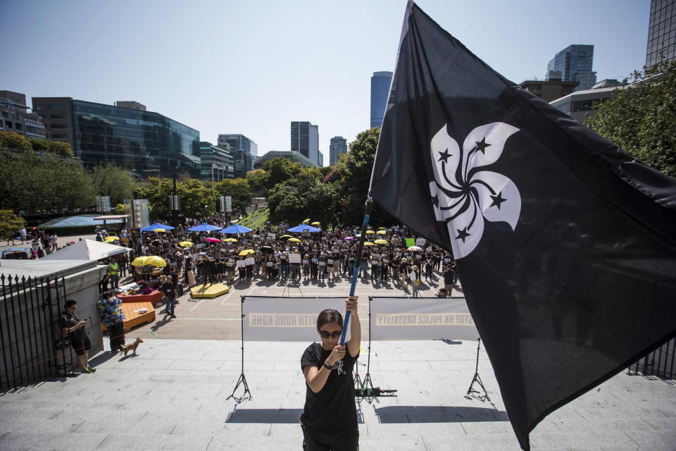 FILE - In this Aug. 3, 2019, file photo, a woman holds a "Black Bauhinia" flag, a symbol of the Hong Kong rebellion, during a rally in support of Hong Kong anti-extradition bill protesters, in Vancouver, British Columbia. Governments around the world are taking a cautious approach to responding to the protests roiling Hong Kong. With the notable exception of Taiwan, cautious comments from a handful of governments fall short of support for the demonstrators. They are so mild that even the word “protest” itself was left out of the joint EU-Canada statement that was the most recent to infuriate the Chinese government. Most are unwilling to risk that fury at all, showing China’s deep influence around the world.(Darryl Dyck/The Canadian Press via AP)