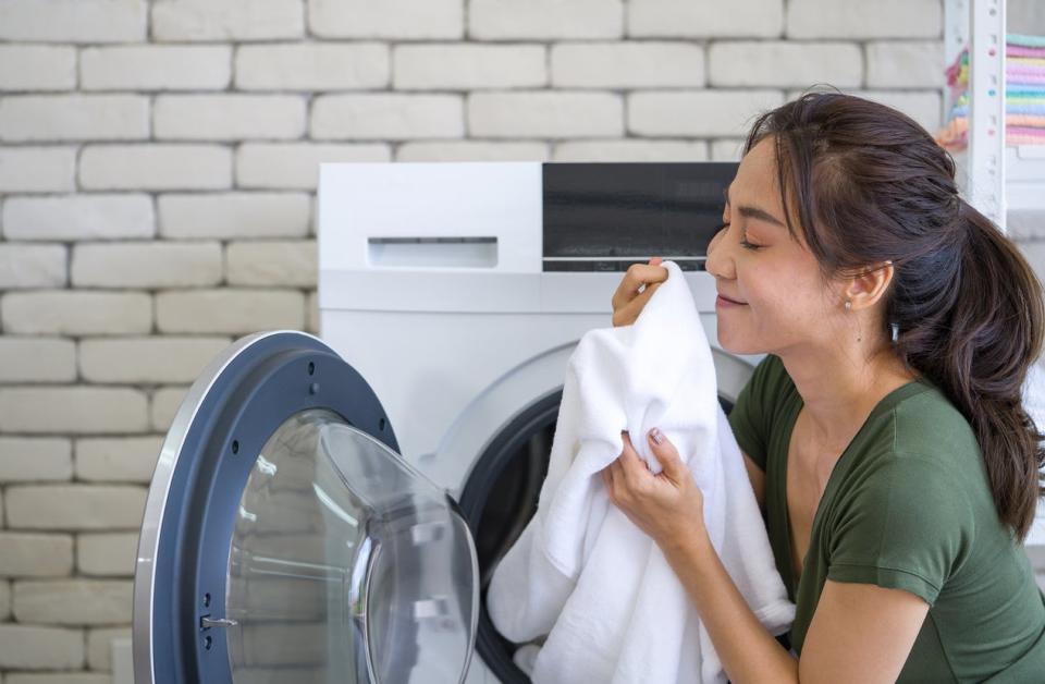 Asian woman inhaled the smell of white cloth that was just washed from the washing machine. Working atmosphere in the laundry room