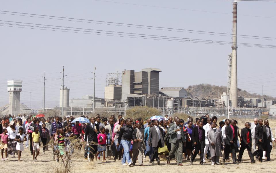 A group of churchgoers proceed to the site, Sunday Aug. 19, 2012 at the Lonmin platinum mine, background, near Rustenburg, South Africa, for a memorial service for 34 dead striking miners who were shot and killed bt police last Thursday. Miners must return to work Monday or face being fired from the mine where rivalry between unions has exploded into violence. (AP Photo/Denis Farrell)