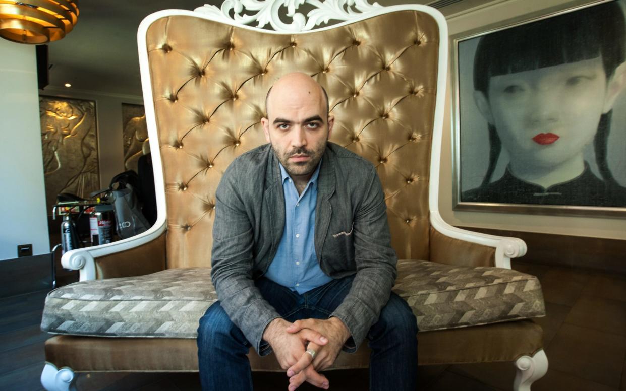Mr Saviano sits on a throne-like chair, unshaven and looking directly into the camera