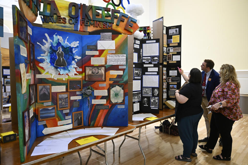 Judges Stefanie Mathew, left, Cody Ingraham, and Patrice Richter, right, examine one of the many historical exhibits by high school students on display at the National History Day event at the University of Maryland, Tuesday, June 11, 2024 in College Park, Md.. (AP Photo/John McDonnell)