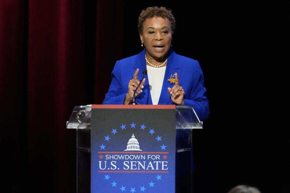 A woman in a blue jacket and white top speaks at a lectern.