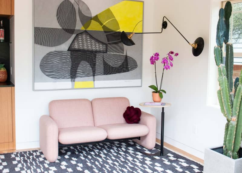 Pink love seat next to side table topped with orchid.