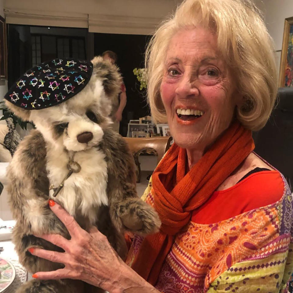 Lillian Frank dressed in bright orange, red and yellow holds up a dog who is wearing a little hat