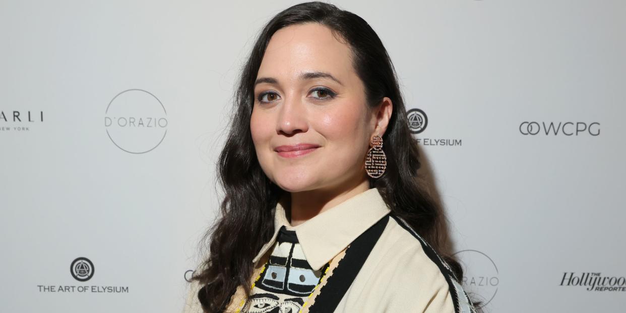 lily gladstone poses on the red carpet wearing a cream, collared jumper with embroidered motifs