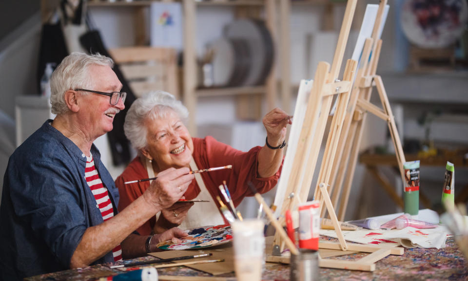 Cheerful elderly couple painting with paintbrushes at art workshop.