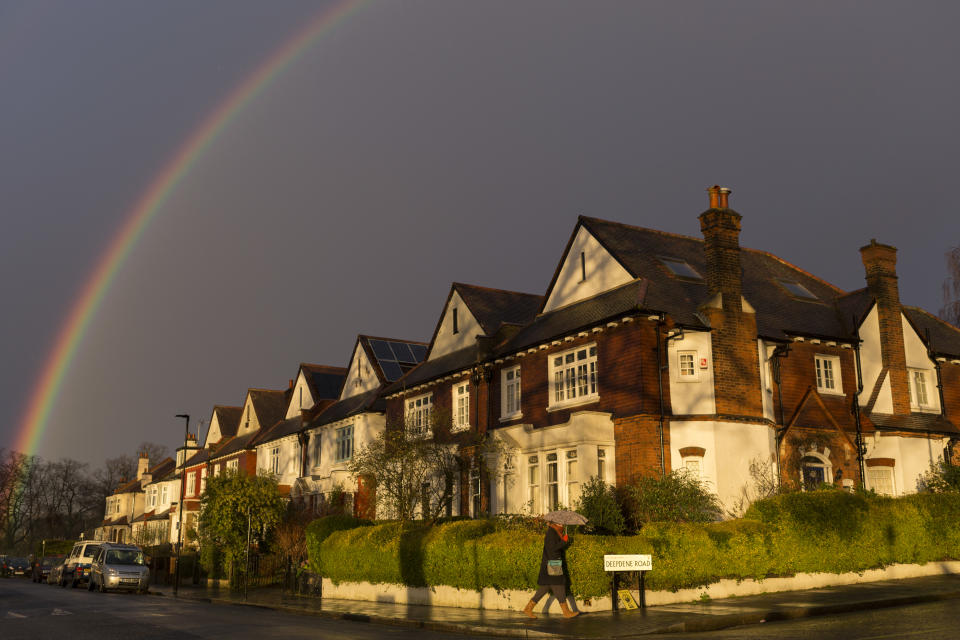 With a brief rainbow arcing overhead, a pedestrian carrying an umbrella walks along a south London residential street, passing sunlit Edwardian period homes after heavy rainfall, on 25th February 2020, in London, England.  (Photo by Richard Baker / In Pictures via Getty Images)