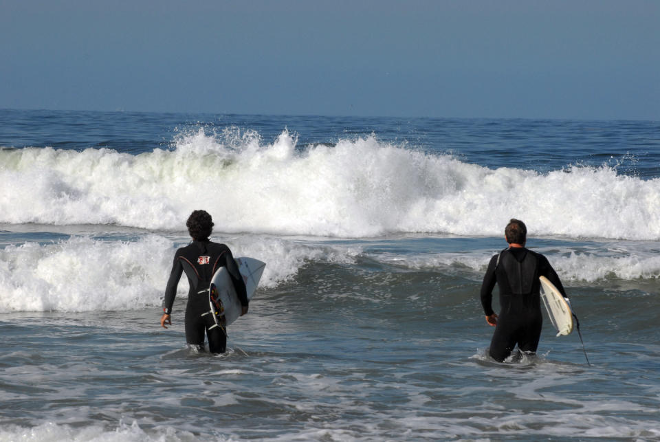Two surfers stand in water, watching the waves come in.