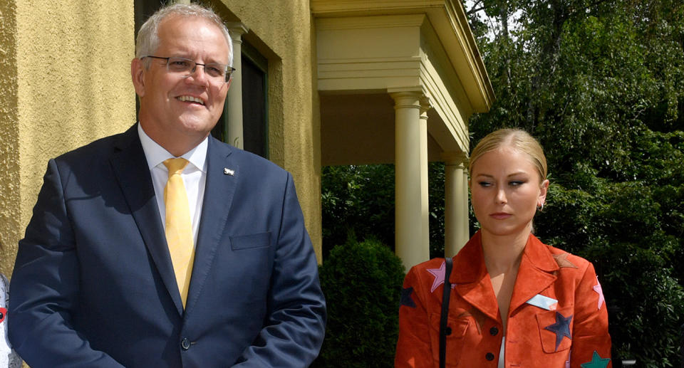 Prime Minister Scott Morrison smiles next to 2021 Australian of the Year Grace Tame, who looks uncomfortable and refrains from smiling.
