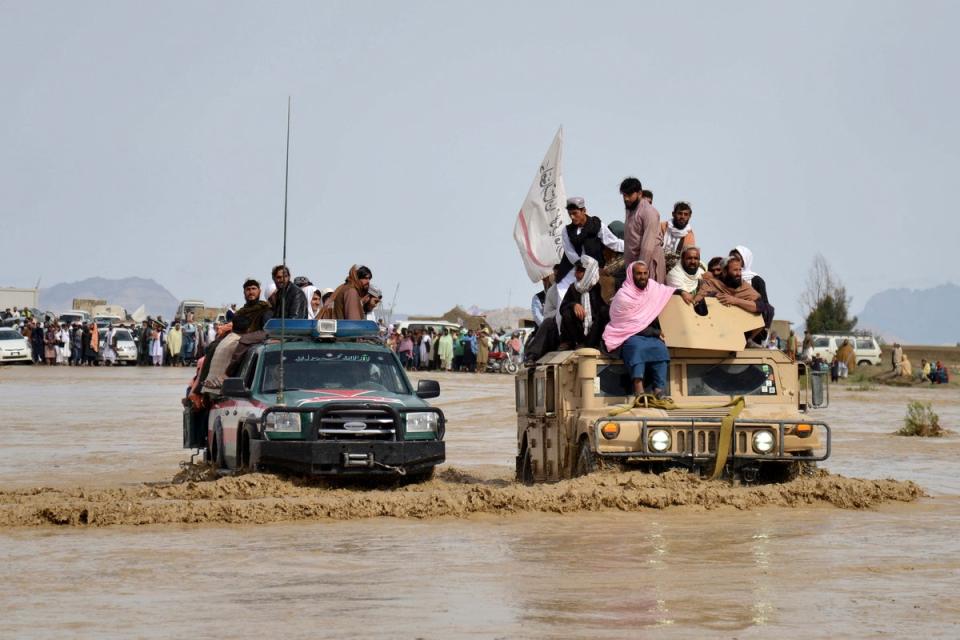 Afghan men sit atop military vehicles as they cross a flooded area in Kandahar province on Saturday (AFP via Getty Images)