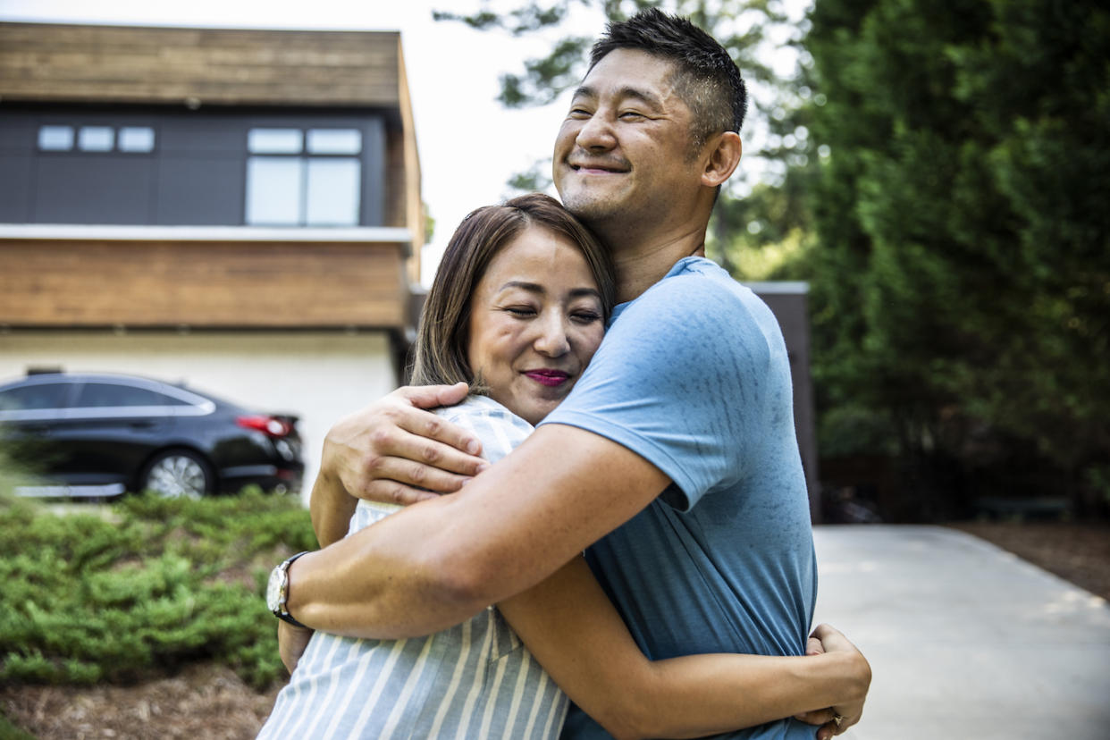 A husband and a wife embracing in front of their modern home