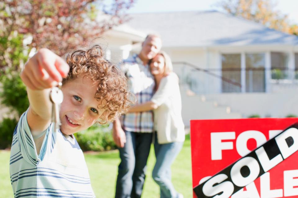 Family standing in front of sold house holding a key.