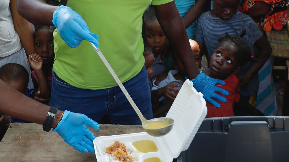 A server ladles soup into a container as children line up to receive food at a shelter for families displaced by gang violence, in Port-au-Prince, Haiti, Thursday, March 14, 2024. - Odelyn Joseph/AP