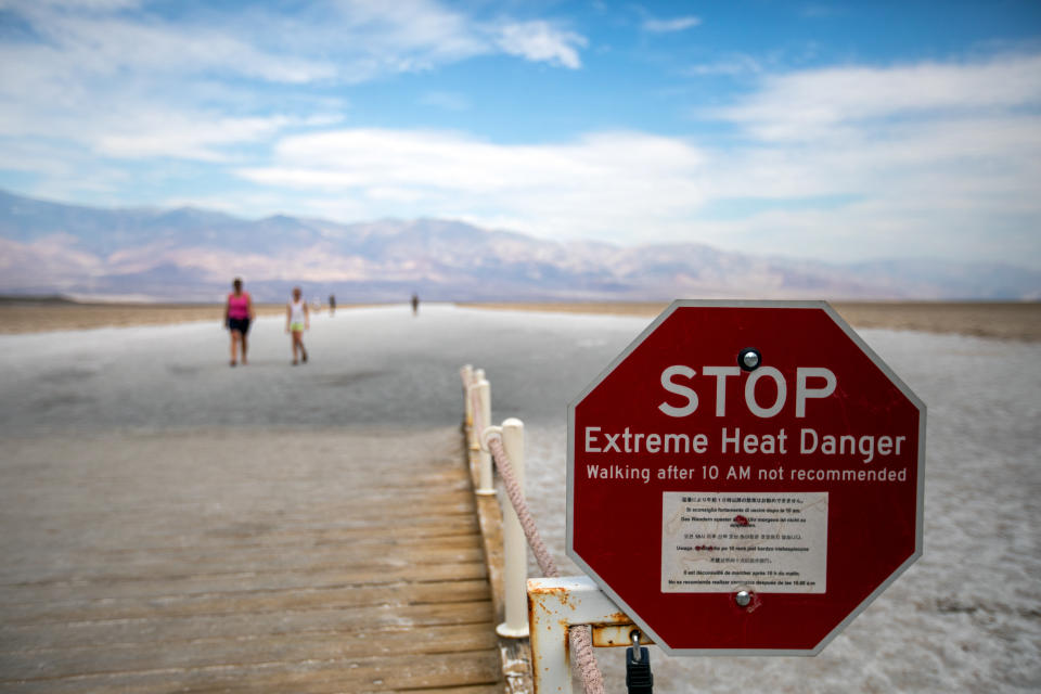 Stop sign with desert landscape in background that reads: Stop, extreme heat danger. Walking after 10 AM not recommended.