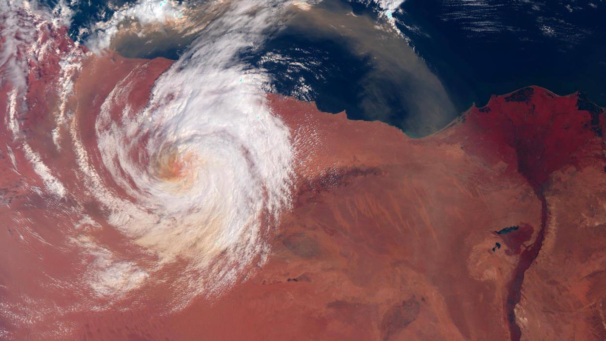  a white-clouded hurricane swirls above the reddish-brown sahara desert and blue mediterranean sea in a satellite photo 