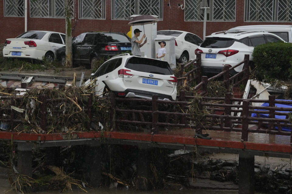 A man and child react near a vehicle washed away by flood waters in the Mentougou district on the outskirts of Beijing, Tuesday, Aug. 1, 2023. Chinese state media report some have died and others are missing amid flooding in the mountains surrounding the capital Beijing. (AP Photo/Ng Han Guan)