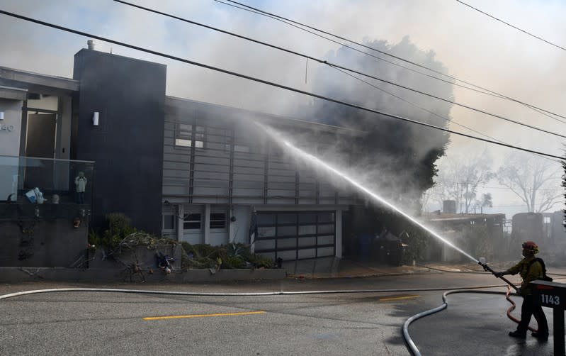 A firefighter douses water on a house to protect it from wind-driven Getty Fire in West Los Angeles, California