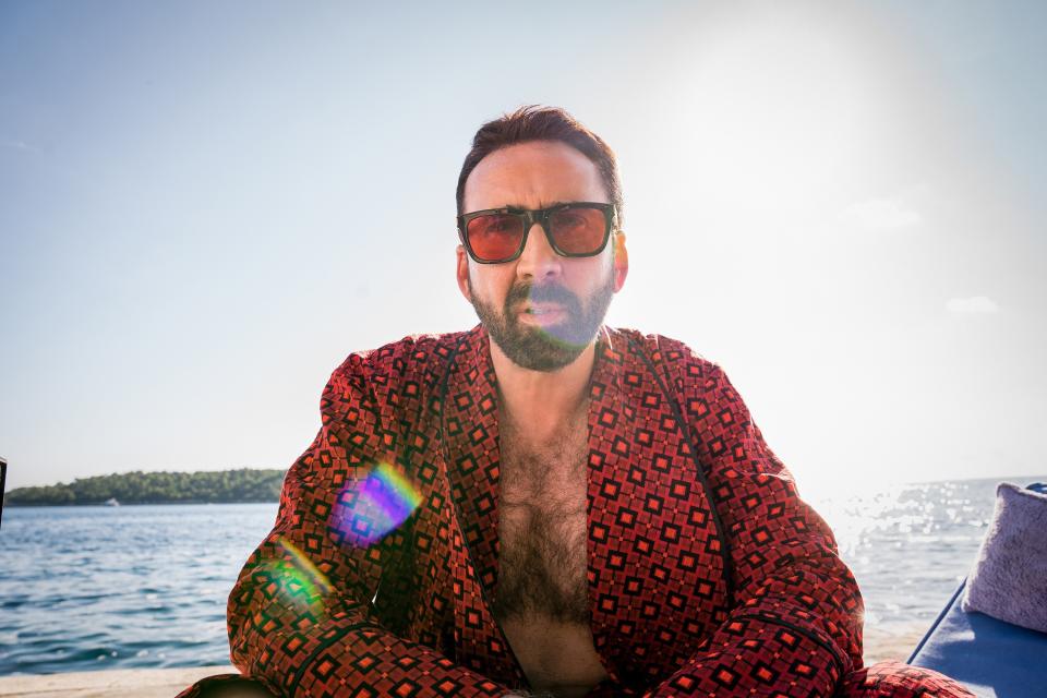 Nicolas Cage sits in a robe by the water