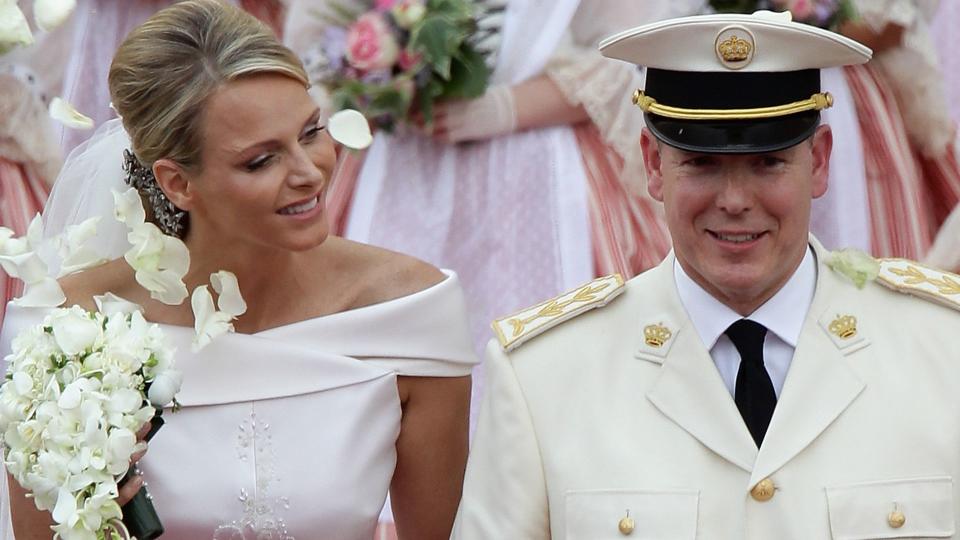 Princess Charlene with her hand through Prince Albert's arm as they're showered with petals following their wedding