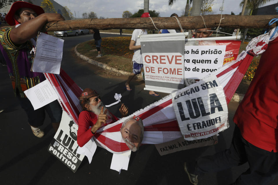 A supporter of Brazil's jailed, former President Luiz Inacio Lula da Silva is carried in a hammock while he is on hunger strike to protest the former leader's corruption conviction, during a march in Brasilia, Brazil, Wednesday, Aug. 15 2018. The Workers’ Party registered da Silva as its candidate for president Wednesday, attempting to muscle him into the race to lead Latin America’s largest nation and forcing a showdown with Brazilian electoral authorities. (AP Photo/Eraldo Peres)