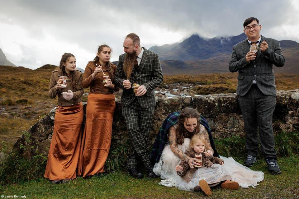 A family eat cake while standing against a wall on the Isle of Skye, Scotland