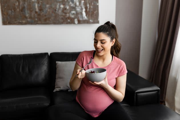 Smiling pregnant woman eating healthy salad at home