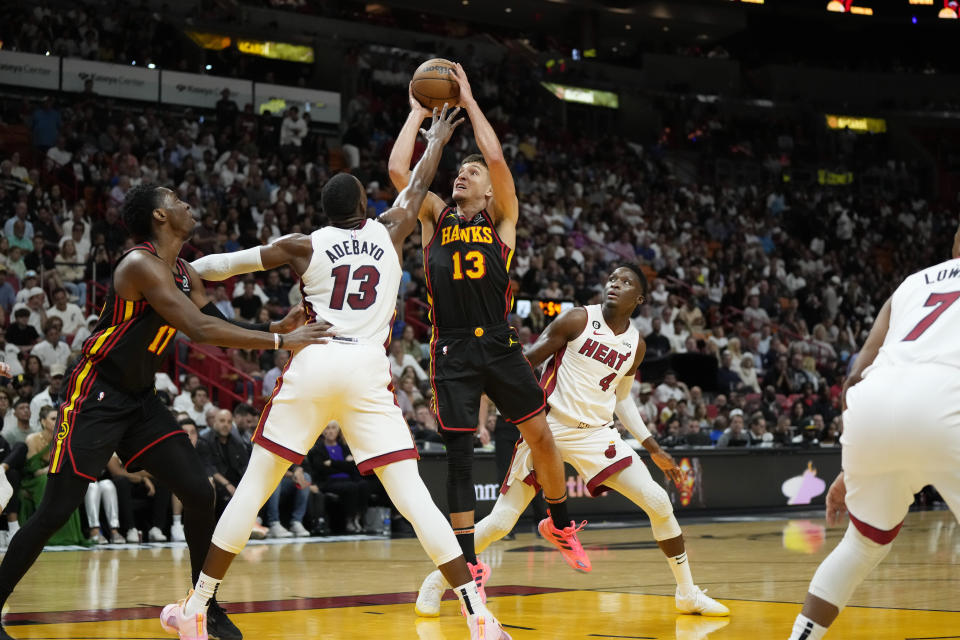 Atlanta Hawks guard Bogdan Bogdanovic (13) shoots from between Miami Heat center Bam Adebayo (13) and guard Victor Oladipo (4) during the first half of an NBA basketball play-in tournament game Tuesday, April 11, 2023, in Miami. (AP Photo/Rebecca Blackwell)