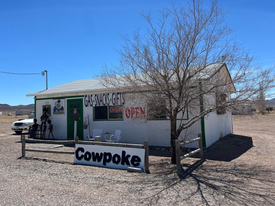 A tiny white building with one sign that reads "Cowpoke" and another that reads "gas, snacks, gifts."