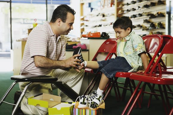 A man helps a young boy try on a pair of shoes in a shoe store.