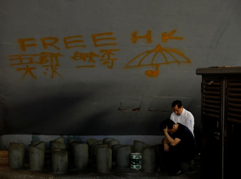 Men take a rest underneath a passengers bridge bearing anti-government graffiti in Hong Kong