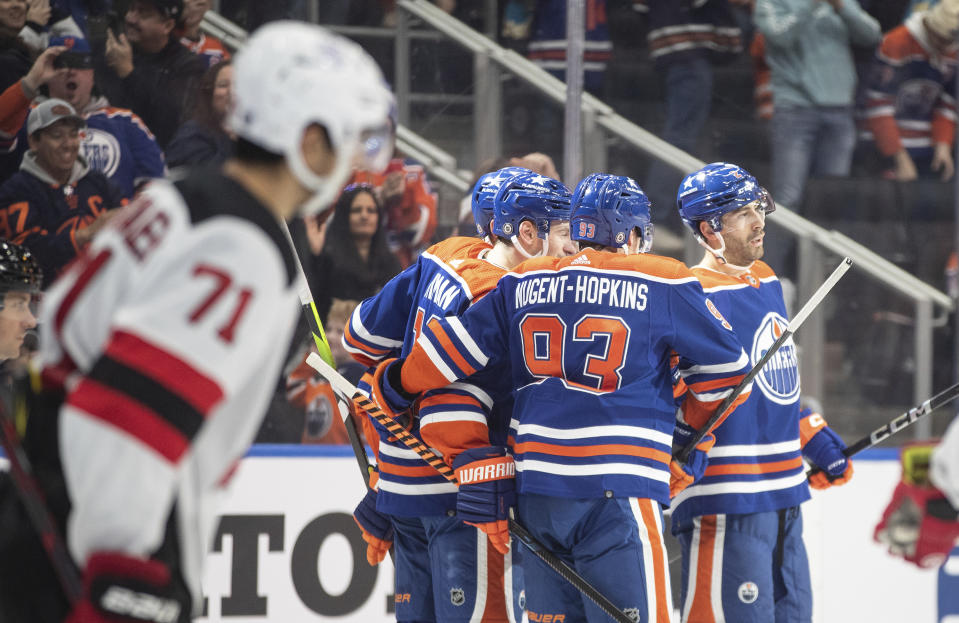 New Jersey Devils' Jonas Siegenthaler (71) looks on as Edmonton Oilers' Zach Hyman (18), Ryan Nugent-Hopkins (93) and Evan Bouchard (2) celebrate after a goal during second-period NHL hockey game action in Edmonton, Alberta, Sunday, Dec. 10, 2023. (Jason Franson/The Canadian Press via AP)