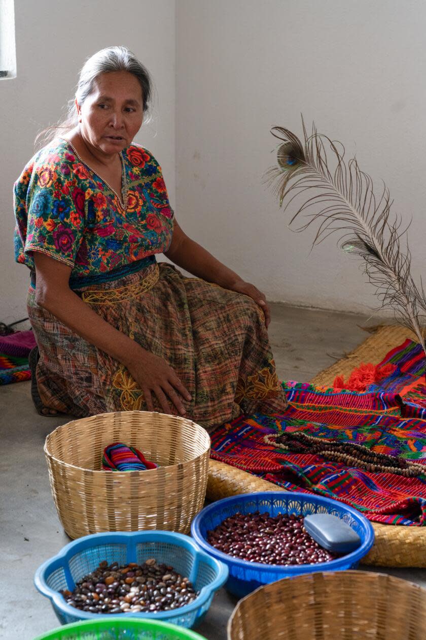 A woman sits on the floor next to baskets of beans and other dry goods
