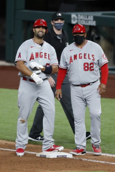 Albert Pujols stands by first base coach Jose Molina smiling.