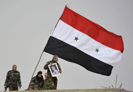 A fighter loyal to Syria's president Bashar Al-Assad holds his picture as fellow fighters rest by a Syrian national flag after gaining control of the area in Deir al-Adas, a town south of Damascus, Daraa countryside February 10, 2015. REUTERS/Stringer