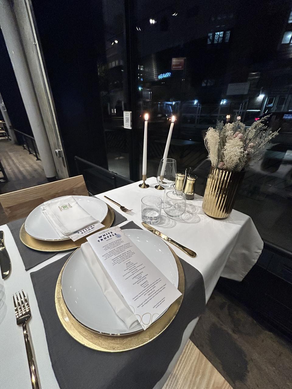 A restaurant table with candles, plates, and White Truffle Menu