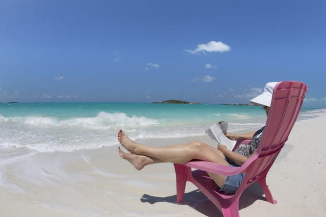 Woman reading in chair on beach, Little Exuma Island, Bahamas