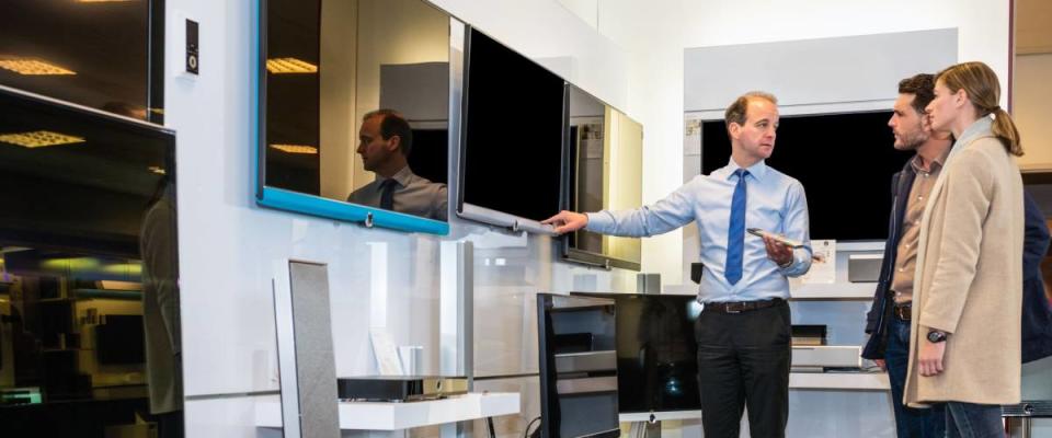 Salesman showing flat screen TV to young couple in electronics store