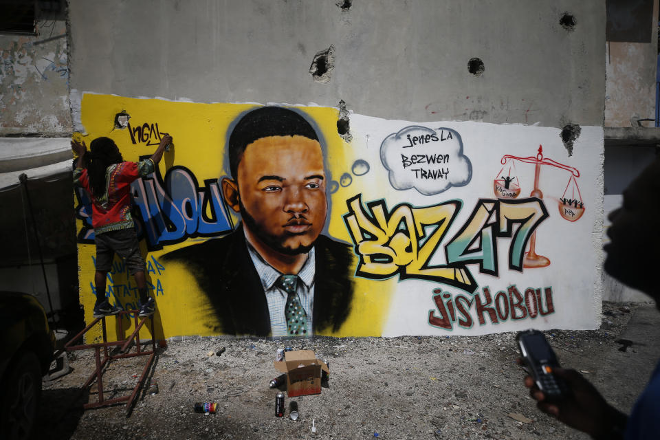 Artist Bungy Baka puts the finishing touches on a mural of opposition community leader Jose Mano Victorieux, known as "Badou," who protestors said was executed Saturday night by unknown assailants. in Port-au-Prince, Haiti, Wednesday, Oct. 2, 2019. A small group of men was protesting at the intersection nearby, blocking a main road with barricades until police intervened. (AP Photo/Rebecca Blackwell)