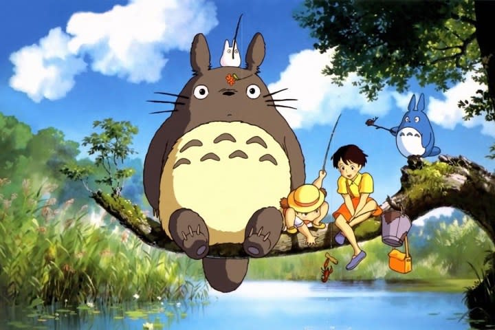 The main characters from My Neighbor Totoro sitting on a tree branch over a river.