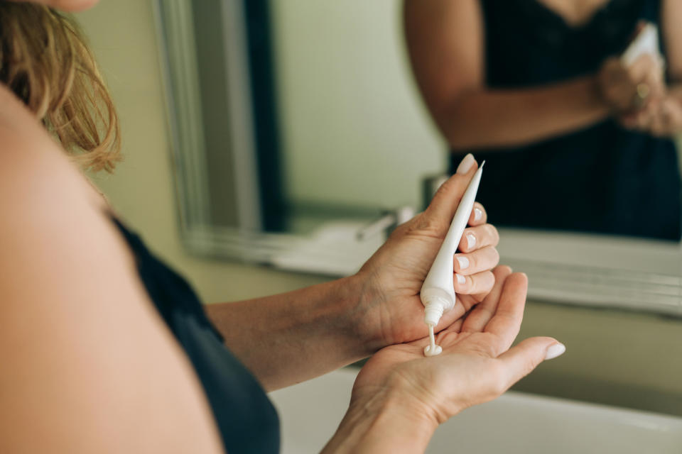 Person applying lotion from a tube to their hand, reflection visible in mirror