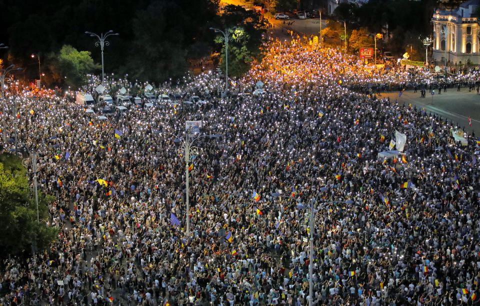 People shine the lights of their mobile phones during a protest outside the government headquarters, in Bucharest, Romania, Saturday, Aug. 11, 2018. Romanians gathered for a second day of protest Saturday, a day after an anti-government protest turned violent leaving 455 people, including three dozen riot police, needing medical treatment. (AP Photo/Vadim Ghirda)