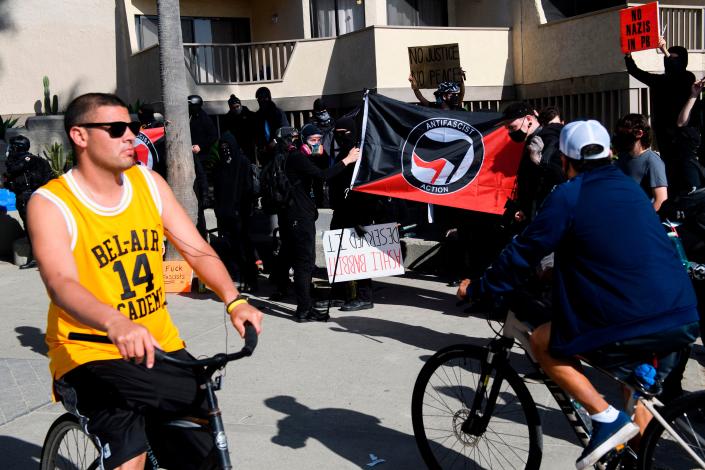 People bicycle past counter-protesters, some holding Antifa flags, awaiting demonstrators for a &quot;Patriot March&quot; demonstration in support of US President Donald Trump on Jan. 9, 2021 in the Pacific Beach neighborhood of San Diego, California.