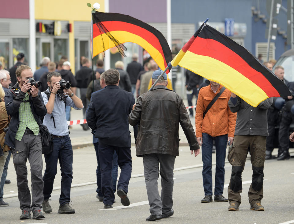 Two men carrying German flags are photographed as they arrive for a demonstration in Chemnitz, eastern Germany, Saturday, Sept. 1, 2018, after several nationalist groups called for marches protesting the killing of a German man last week, allegedly by migrants from Syria and Iraq. (AP Photo/Jens Meyer)