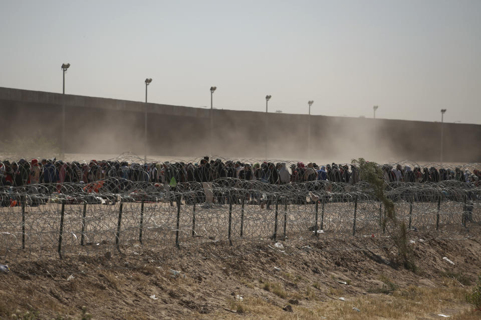 ARCHIVO - Migrantes alineados entre una valla con alambre de púas y el muro fronterizo entre Estados Unidos y México, visto desde Ciudad Juárez, México, el 9 de mayo de 2023. Sin quererlo, las personas migrantes en América Latina financian la desinformación durante sus trayectos hacia Estados Unidos, pues son víctimas de fraudes y engaños que les pueden costar miles de dólares y con los que se sostienen nuevos modelos de negocio, que van desde falsos reclutadores de trabajadores hasta quienes se hacen llamar "coaches de migración". (AP Foto/Christian Chávez, Archivo)