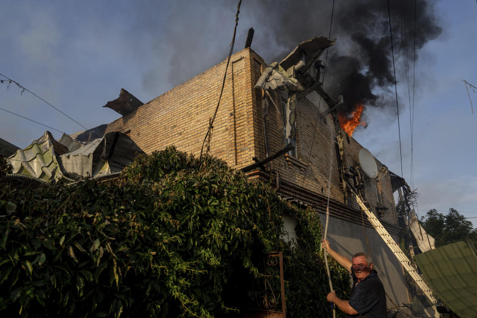 俄軍火砲擊中烏克蘭一處民宅，引發火警，屋主急忙灑水滅火。(畫面來源：AP)