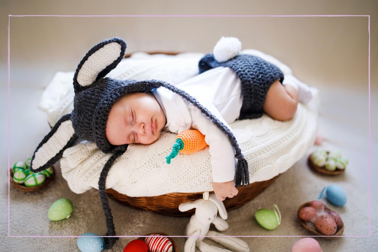  A newborn baby in a basket wearing bunny ears and a tail surrounded by Easter eggs. 