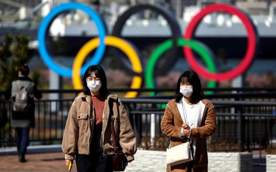 People wearing protective face masks are seen in front of the Giant Olympic rings at the waterfront area at Odaiba Marine Park in Tokyo - REUTERS