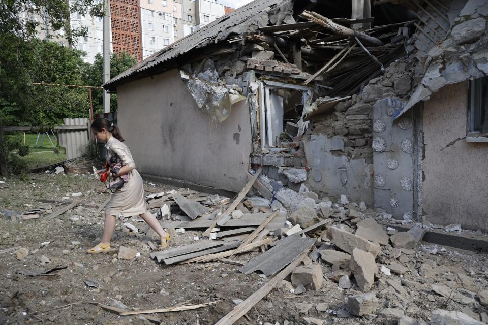 A girl carries a dog as she walks past a house damaged from shelling in the Leninsky district of Donetsk, on the territory which is under the Government of the Donetsk People's Republic control, eastern Ukraine, Monday, June 6, 2022. (AP Photo/Alexei Alexandrov)
