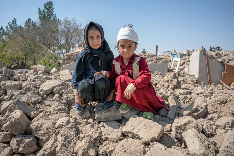 Six-year-old Marzwa (right) sits with her sister, Elina, in the remains of her house wearing a red dress - one of her few possessions that was not buried under the earthquake in Karnil Wardaka village, Zinda Jan District, western Afghanistan.
